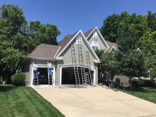A house is being painted by two men on ladders.