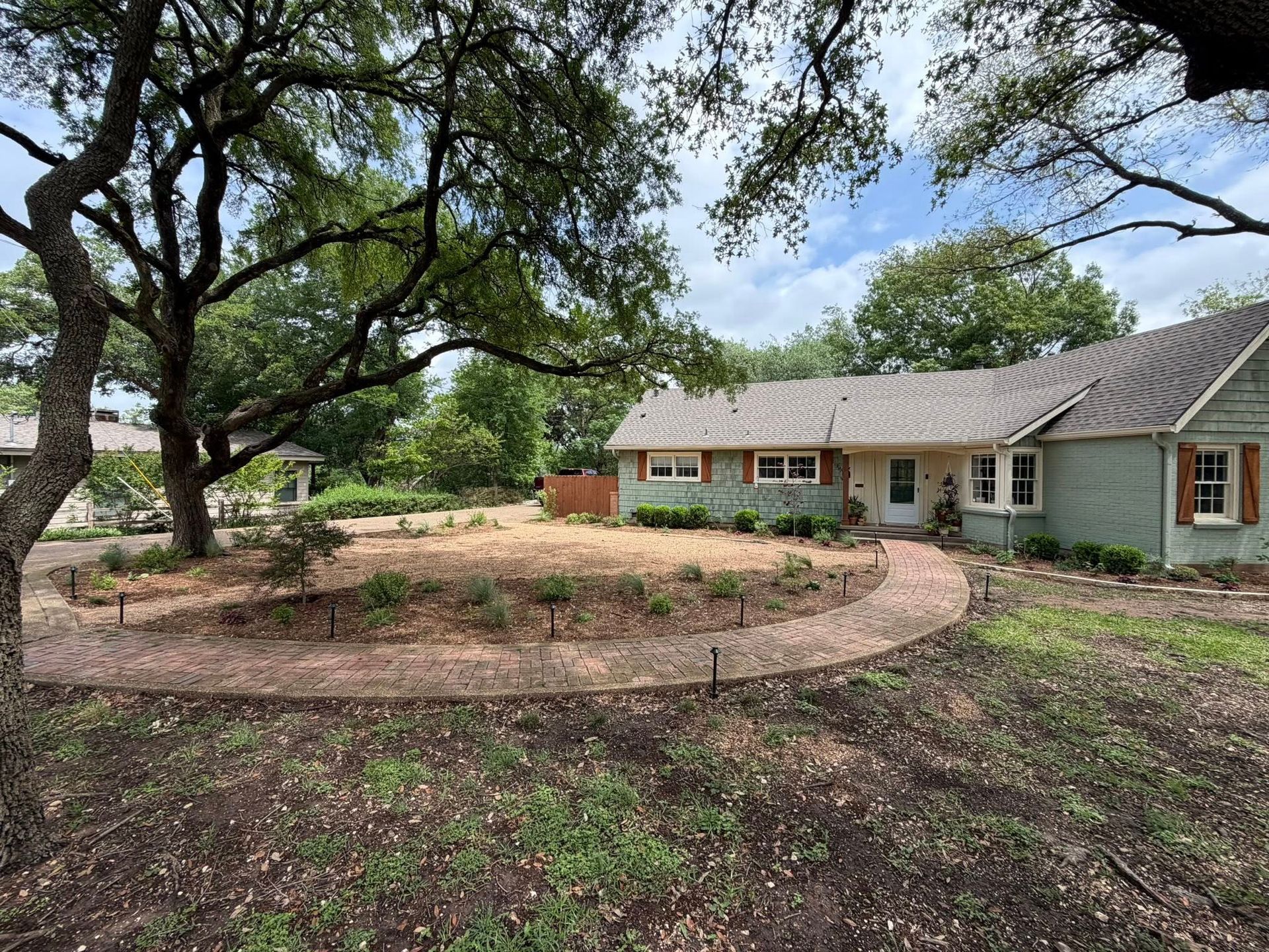 Single-story house with large trees and a curved front walkway in a wooded yard