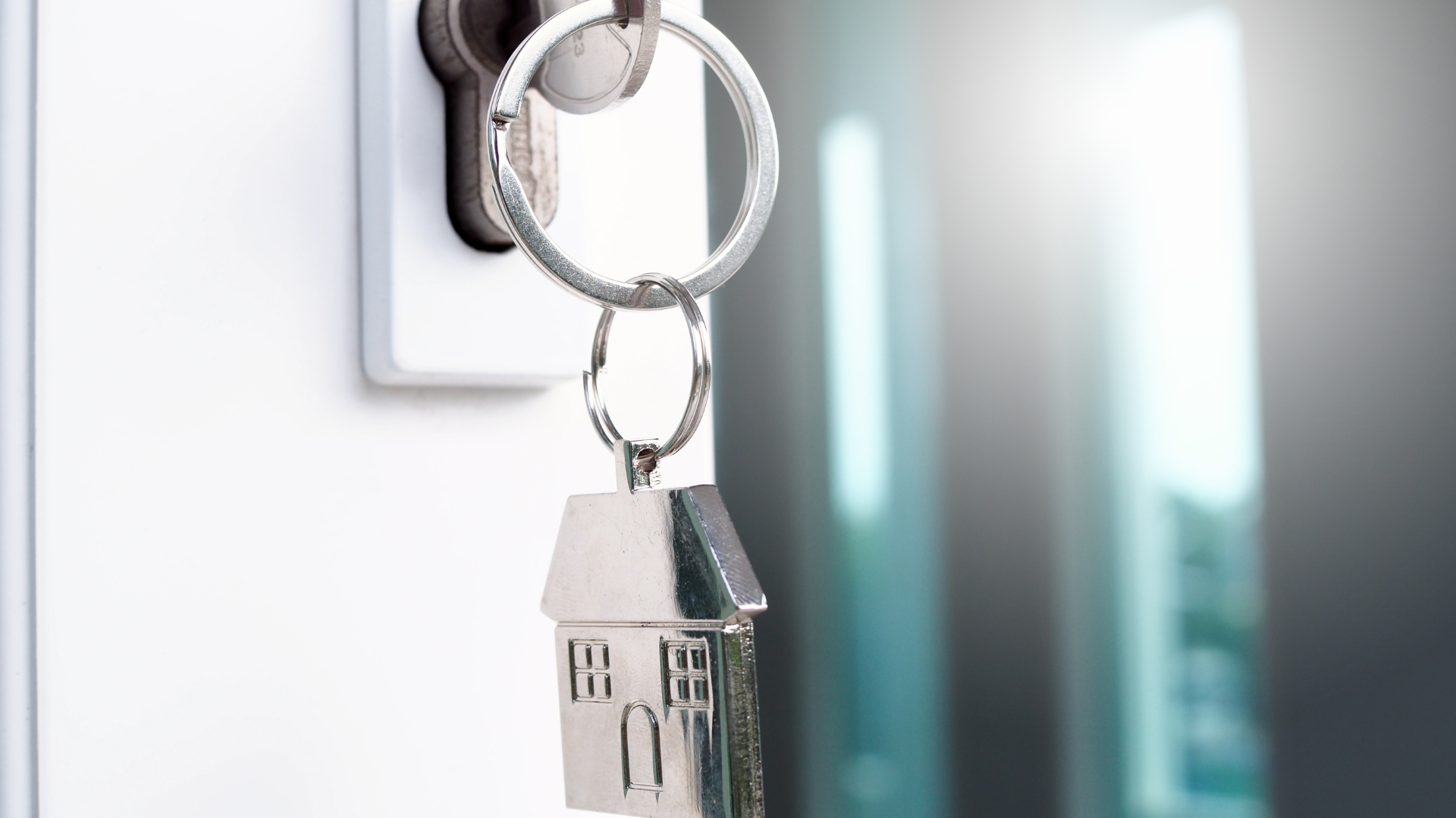 Key in a door, with a house-shaped keychain, in a bright entryway.