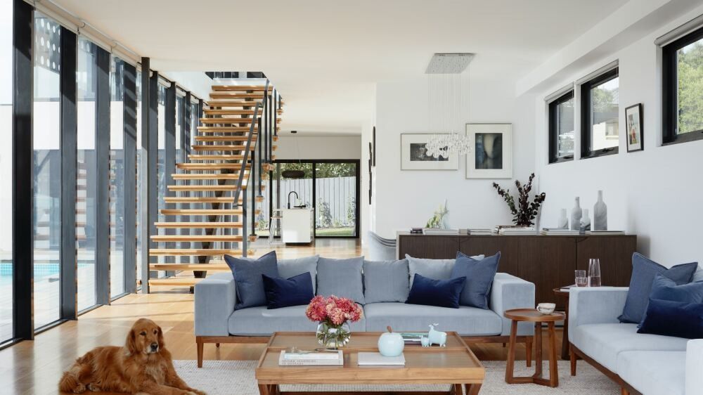 Modern living room with light gray sofas, wooden accents, and a golden retriever dog.