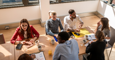 Group of people in a meeting room, sitting at a table with papers, discussing a project.