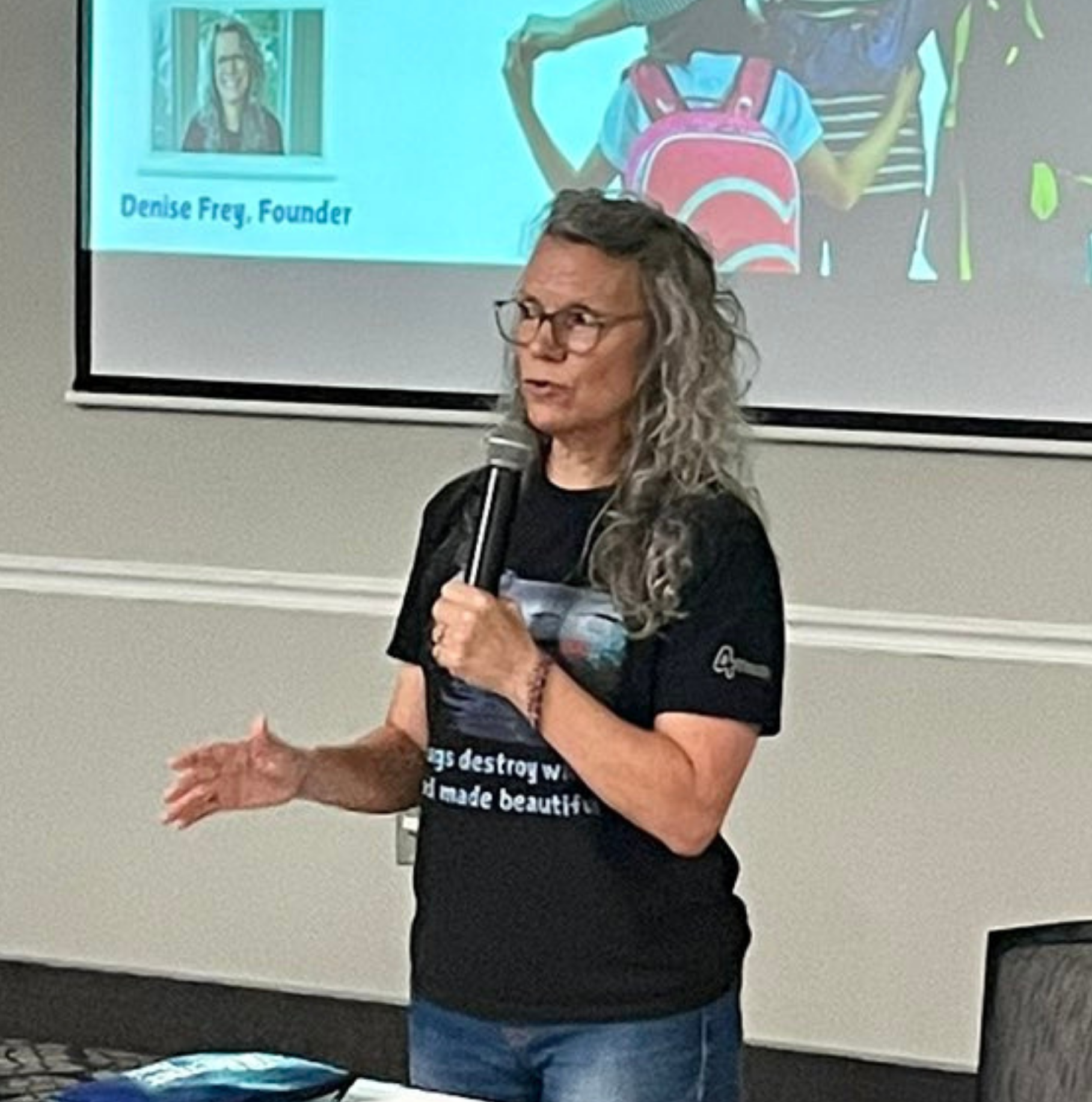 Woman in black dress giving a presentation, gesturing to audience.