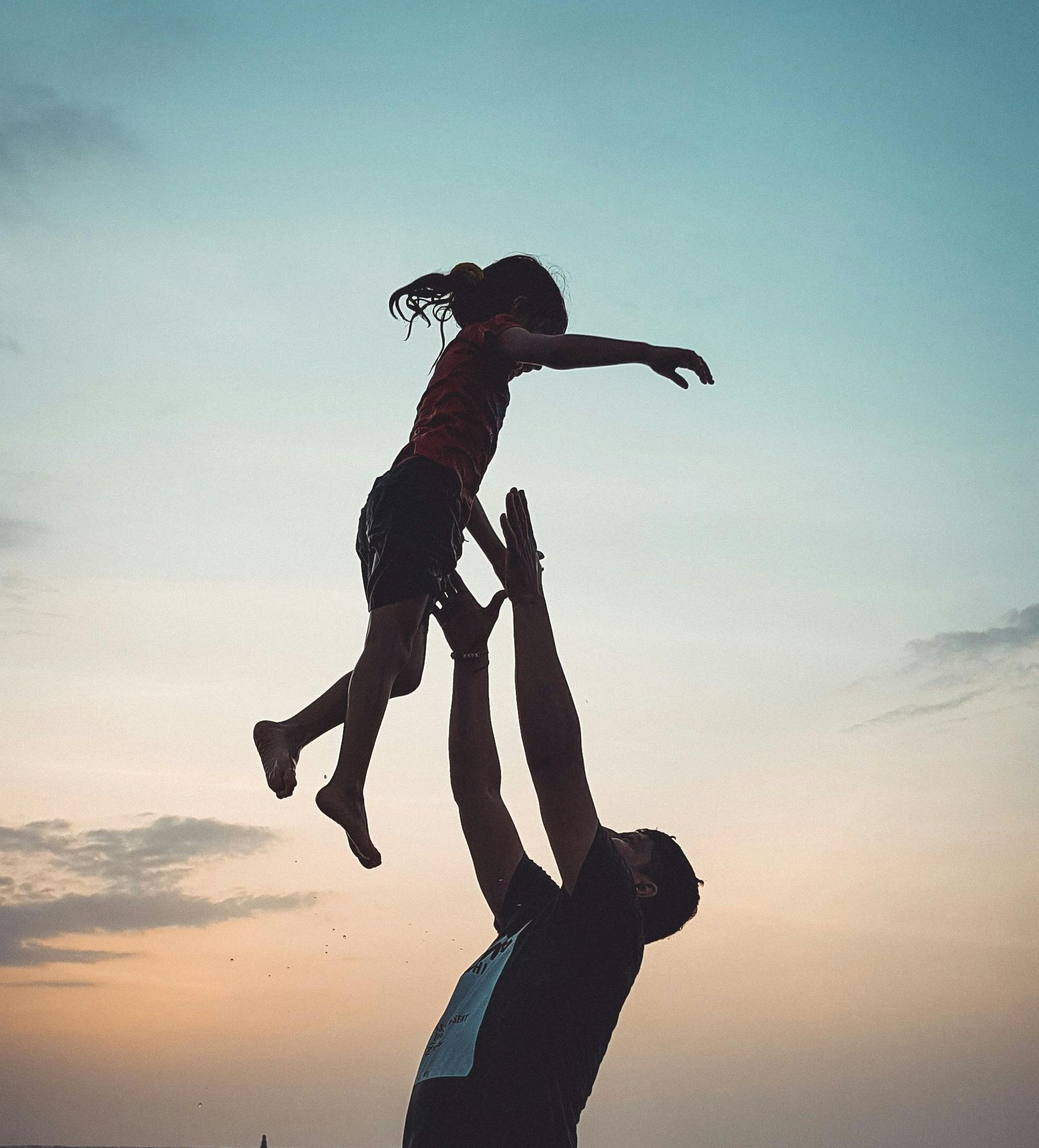 Man throwing a child up in the air at sunset.