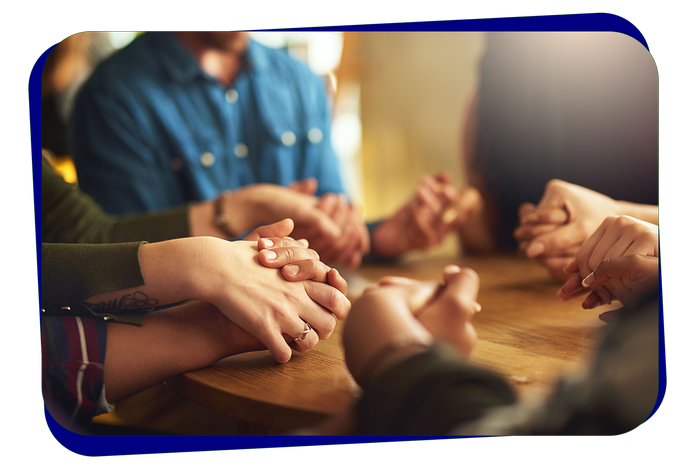 A group of people are sitting at a table holding hands.