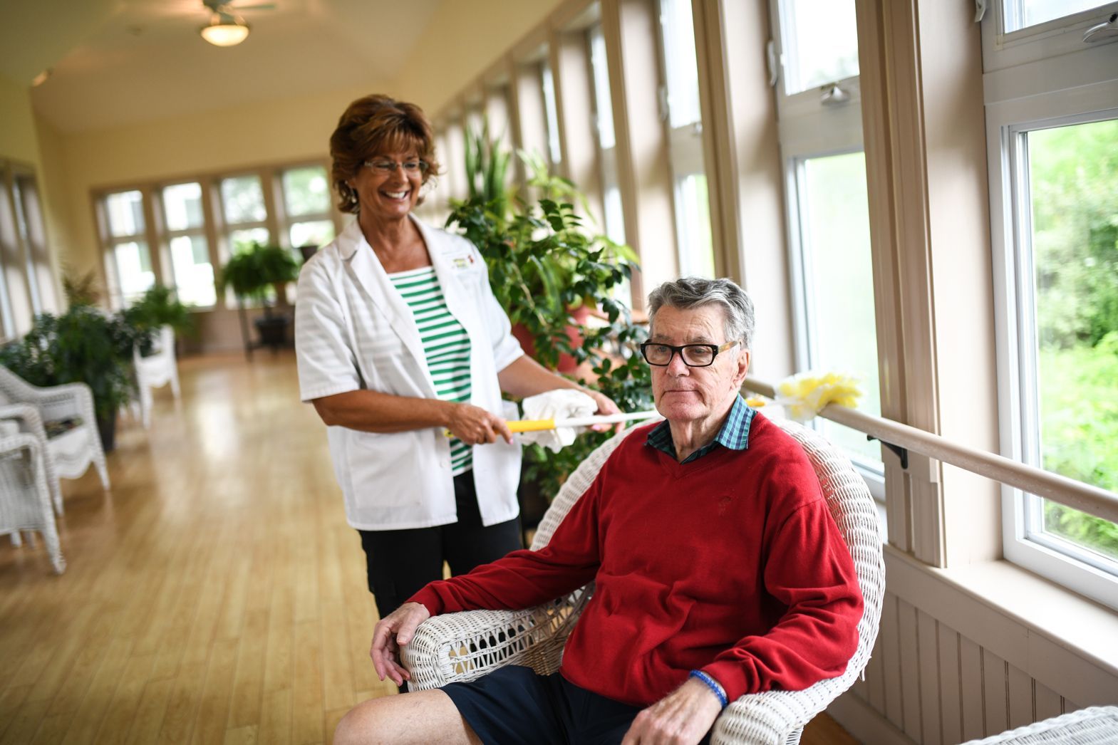 Caregiver standing beside a seated resident in a bright hallway at Watson Assisted Living