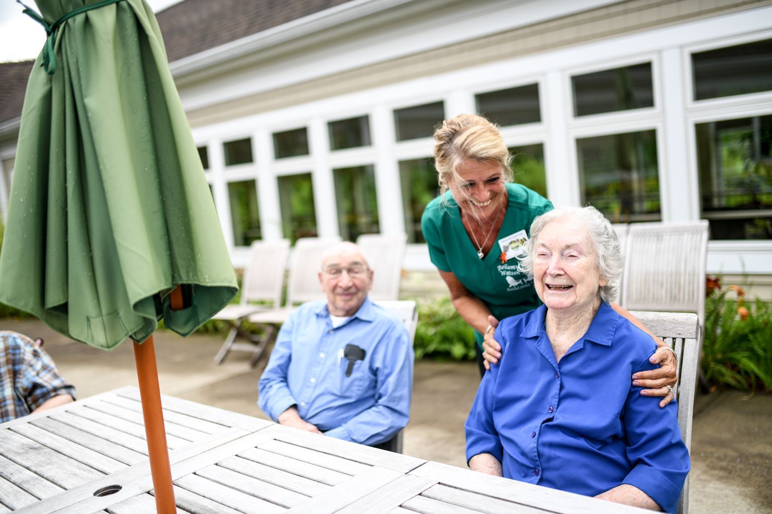 Caregiver assisting two elderly residents outdoors at Watson Assisted Living courtyard