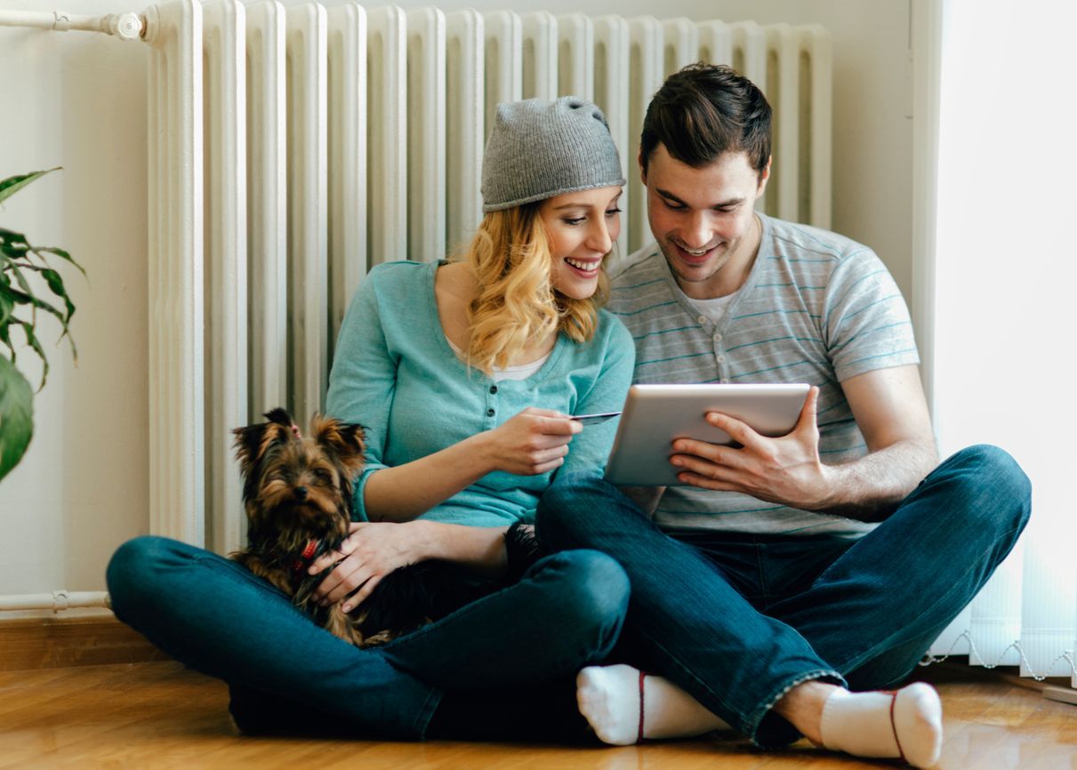 A man and a woman are sitting on the floor looking at a tablet.