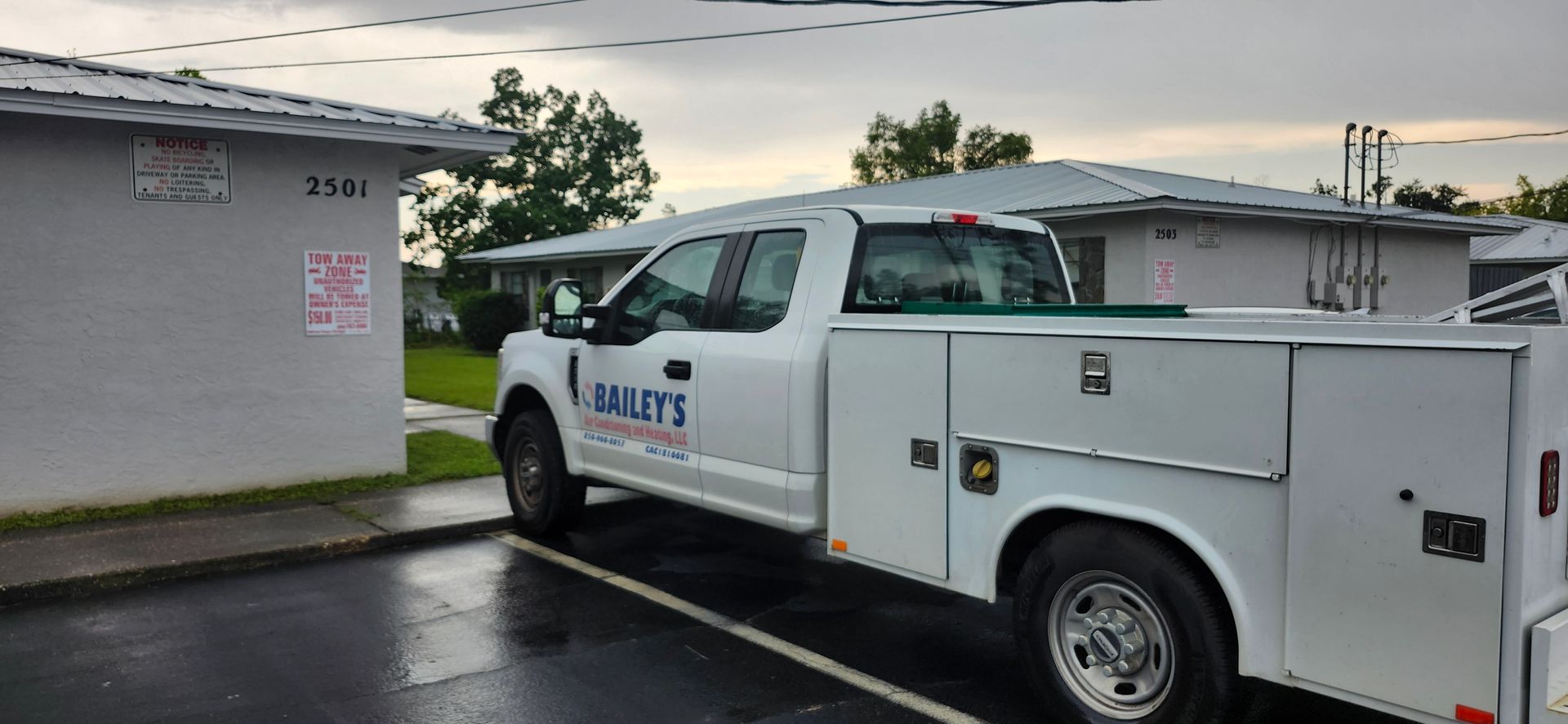 A white utility truck is parked in a parking lot in front of a building.