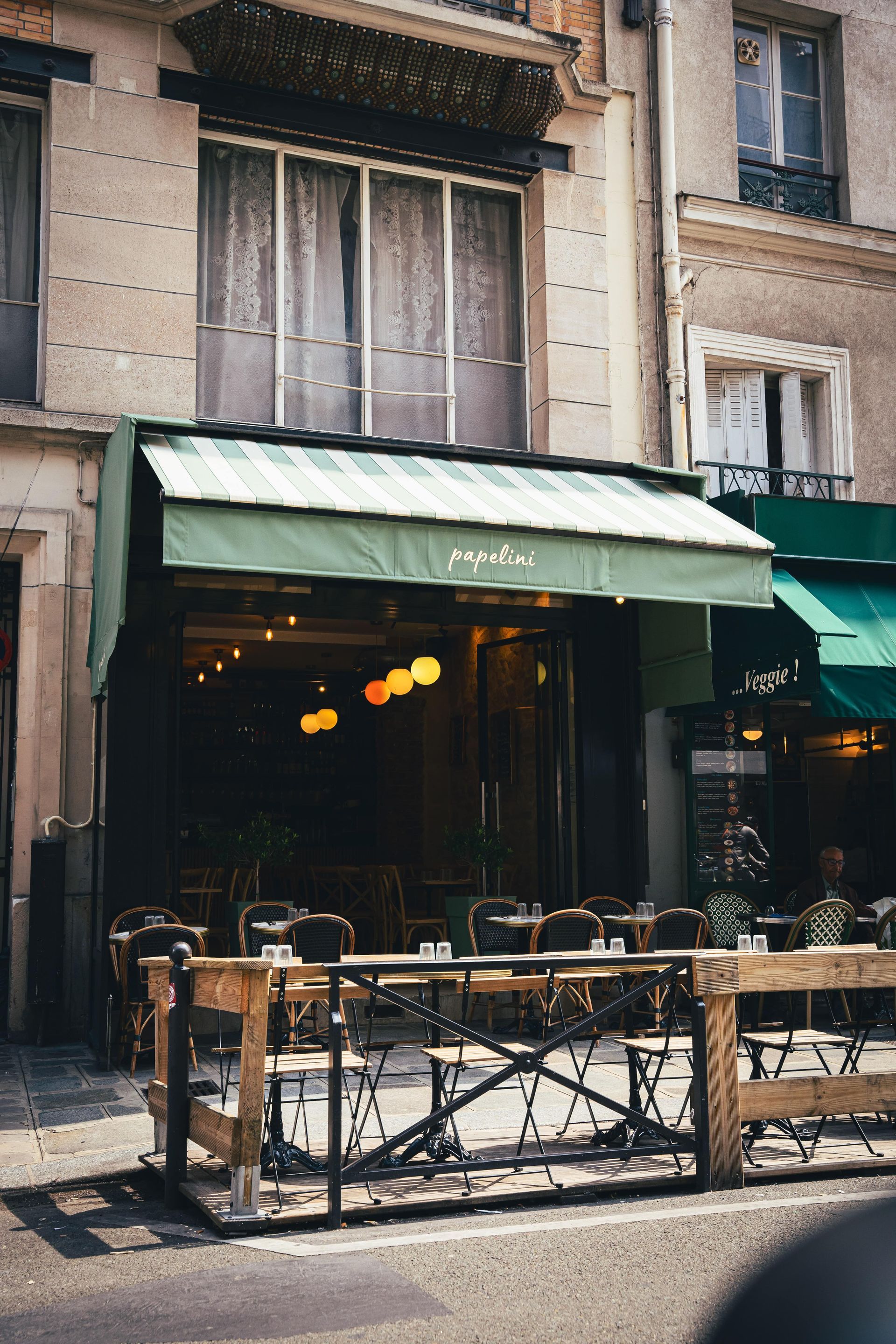 Façade de restaurant avec auvent vert, terrasse et fenêtres.