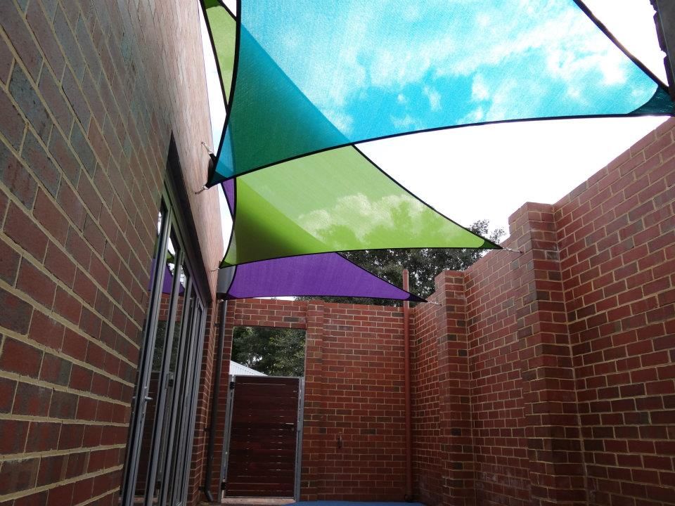 A brick building with a blue green and purple shade sail