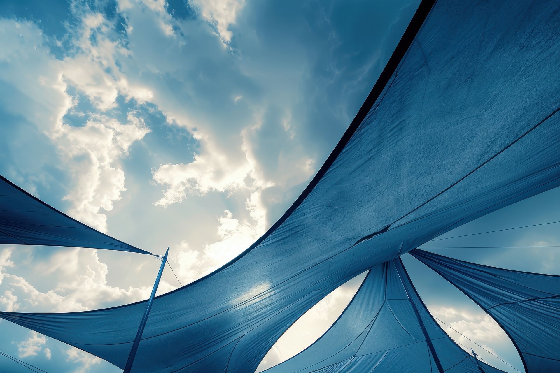 Blue shade sails over outdoor play area against cloudy sky.