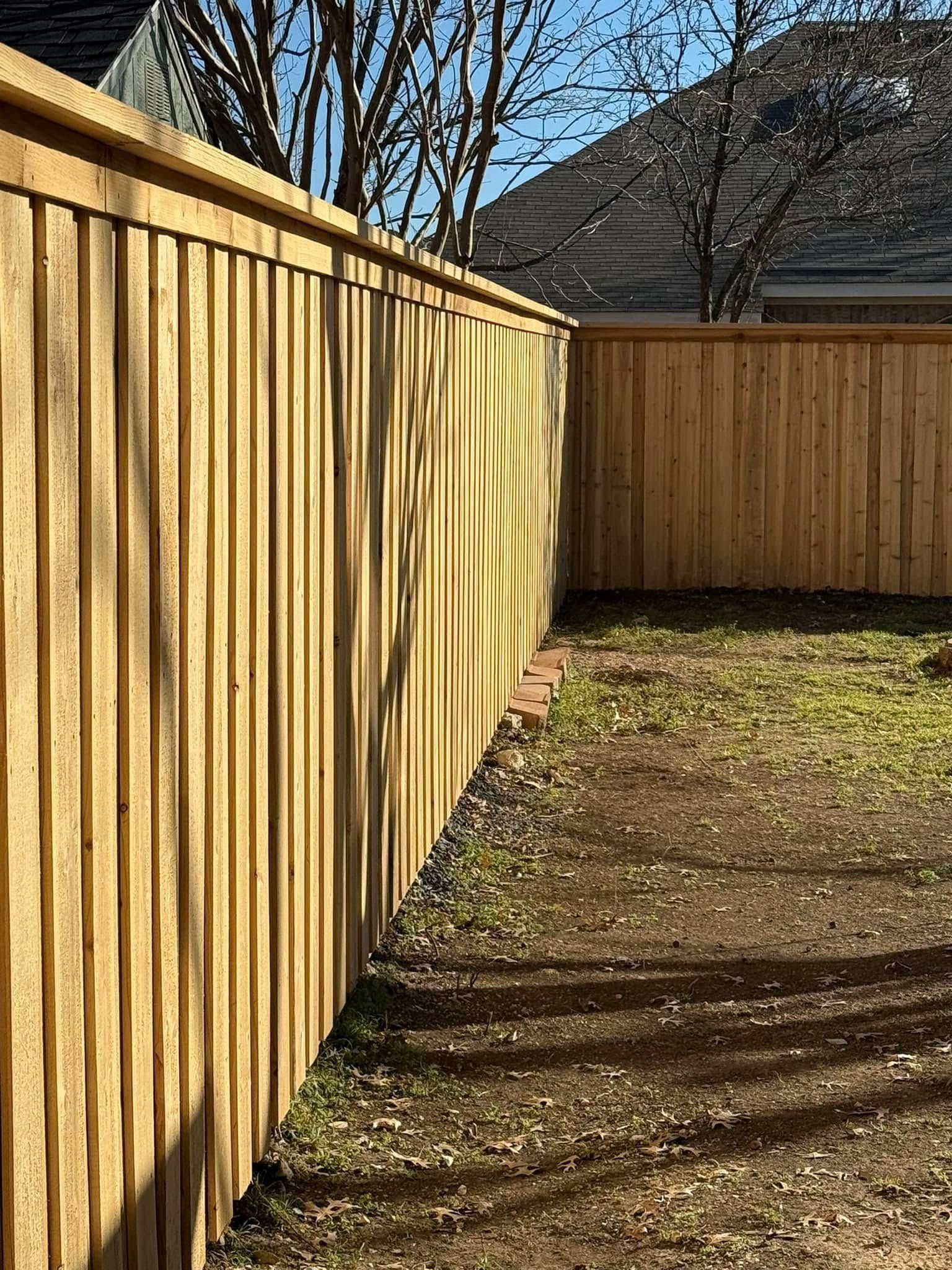A new light-brown wooden fence in an L-shaped corner outdoors on a sunny day.