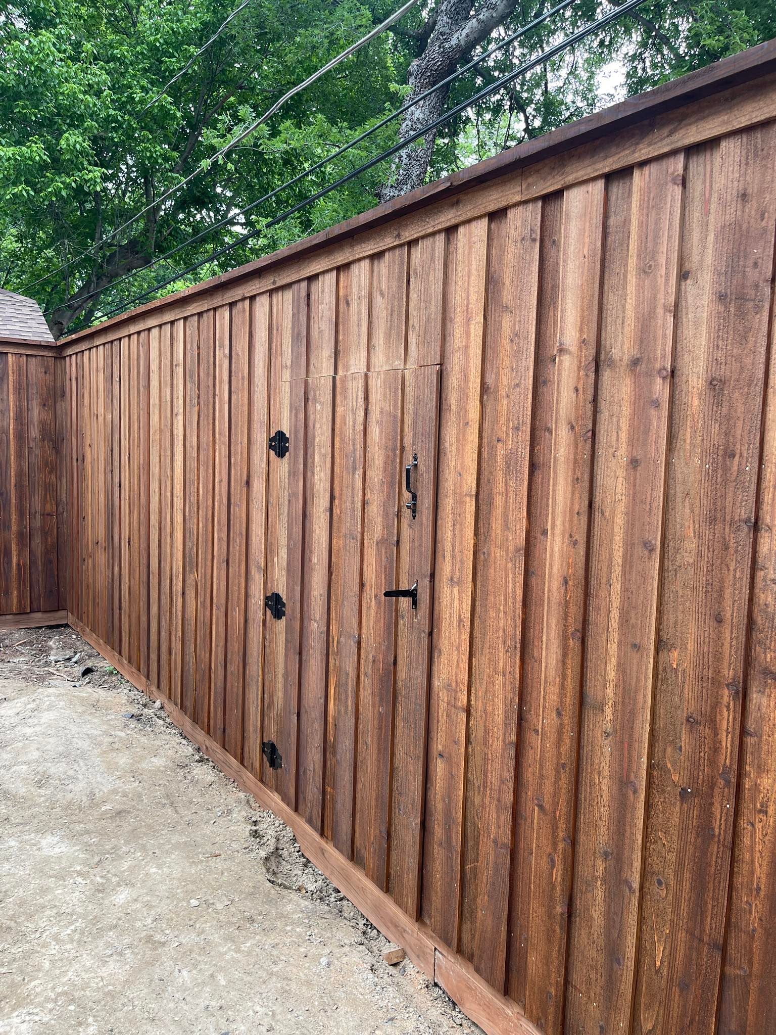 A brown, vertical-slat wooden fence with a matching gate featuring black metal hinges and a latch.
