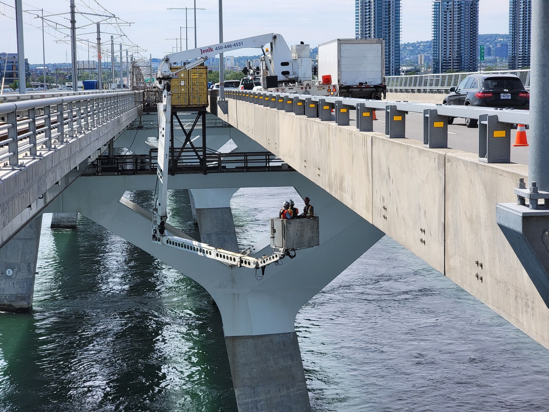 Des ouvriers, à bord d'une plateforme élévatrice mécanique, inspectent la face inférieure d'un pont en béton enjambant l'eau.