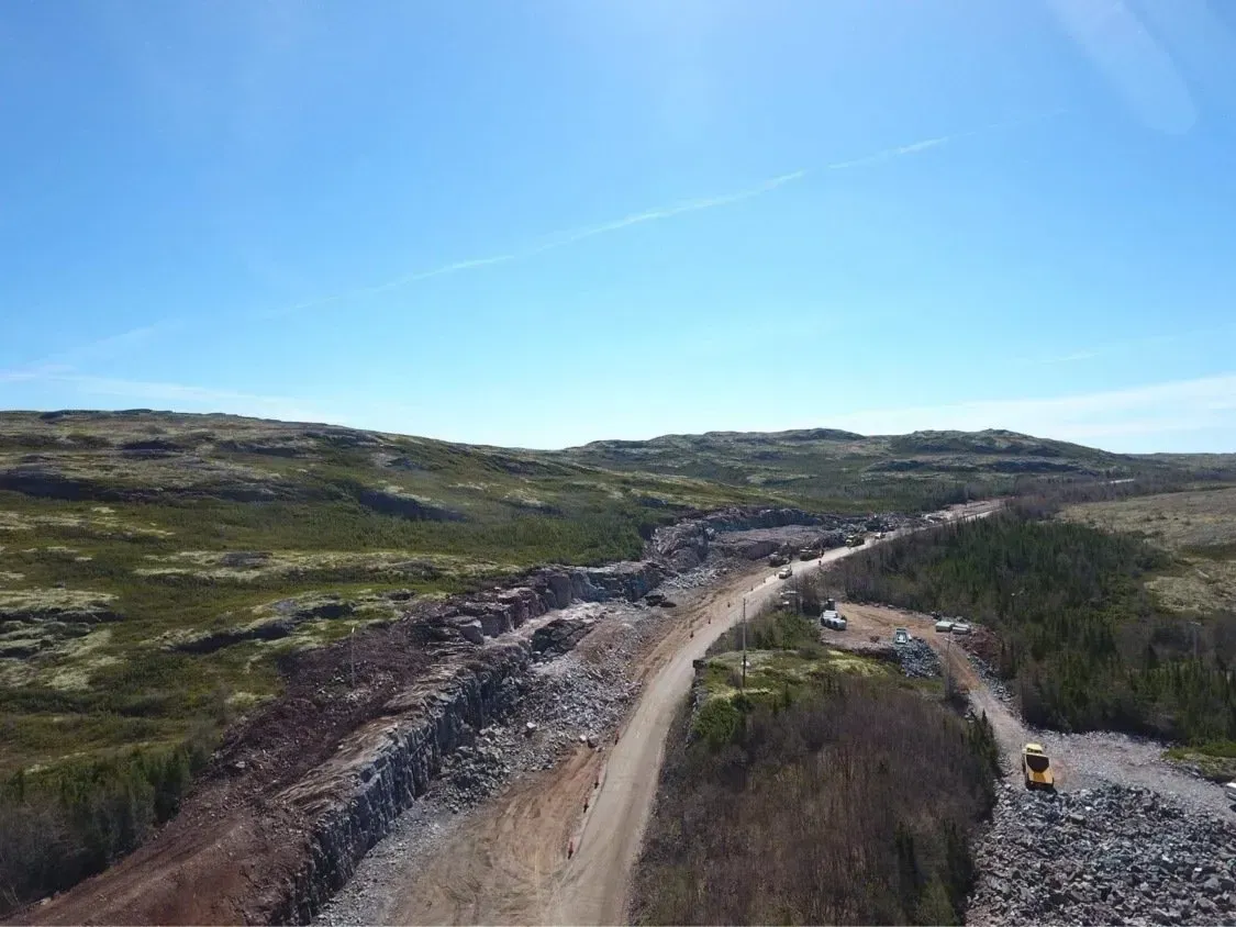 Vue aérienne d'un chemin de terre traversant un paysage accidenté et rocailleux sous un ciel bleu limpide.