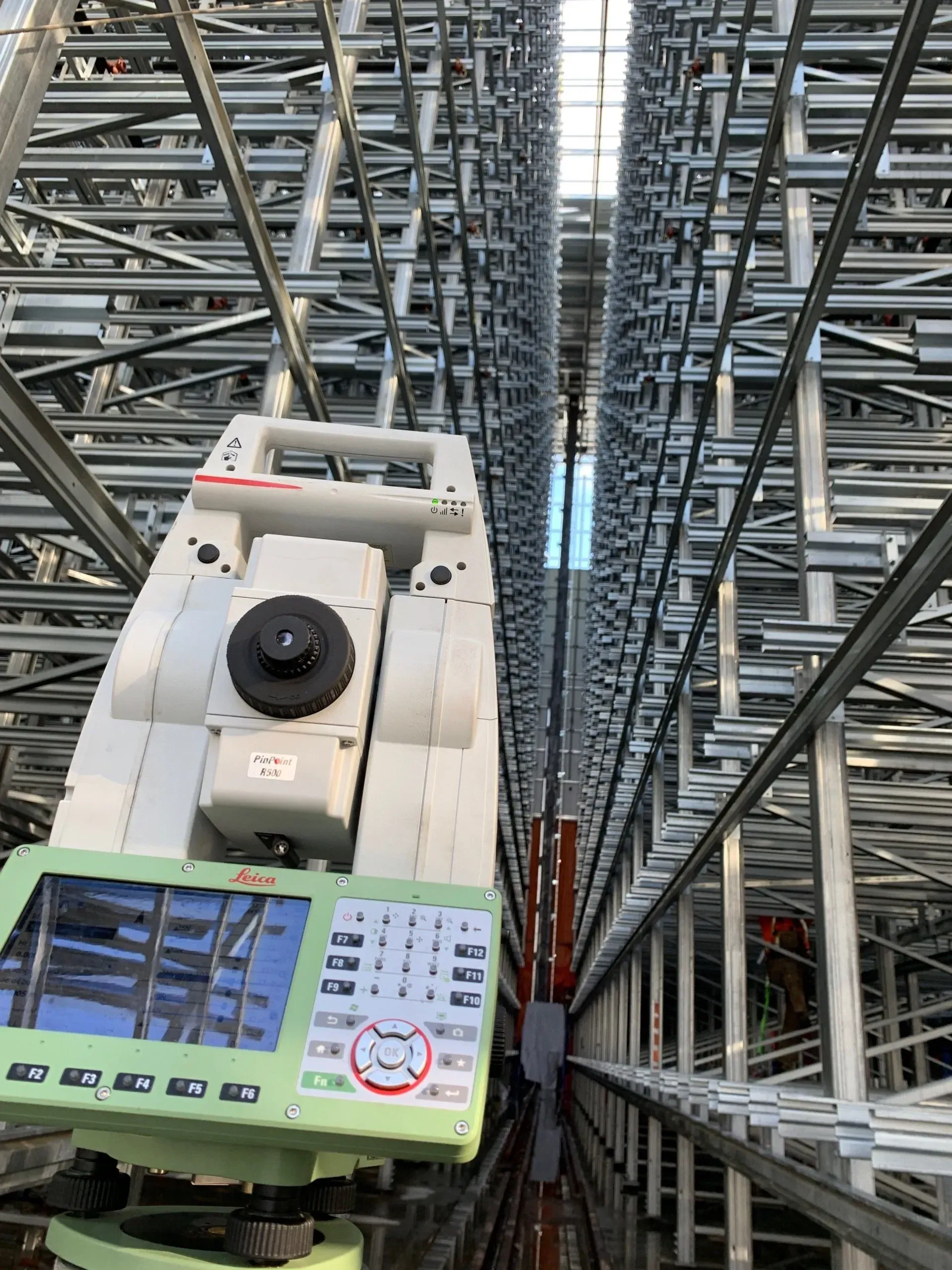 Une station totale de topographie installée entre de hautes rayonnages métalliques d'entrepôt industriel.