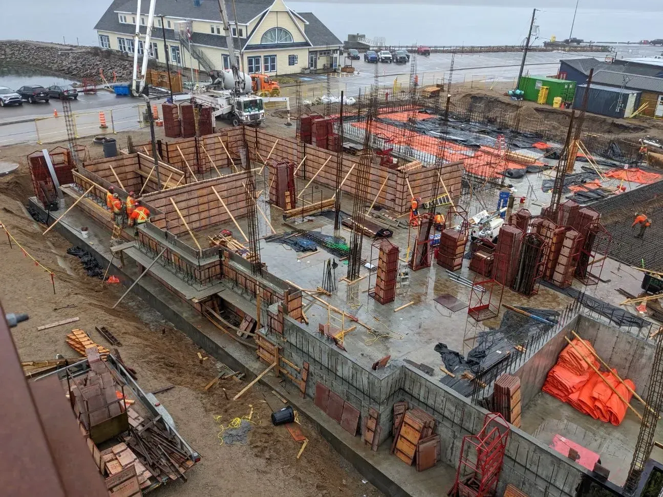 Vue aérienne d'un chantier de construction avec des murs de fondation en béton, des filets de sécurité orange et des ouvriers sur place.