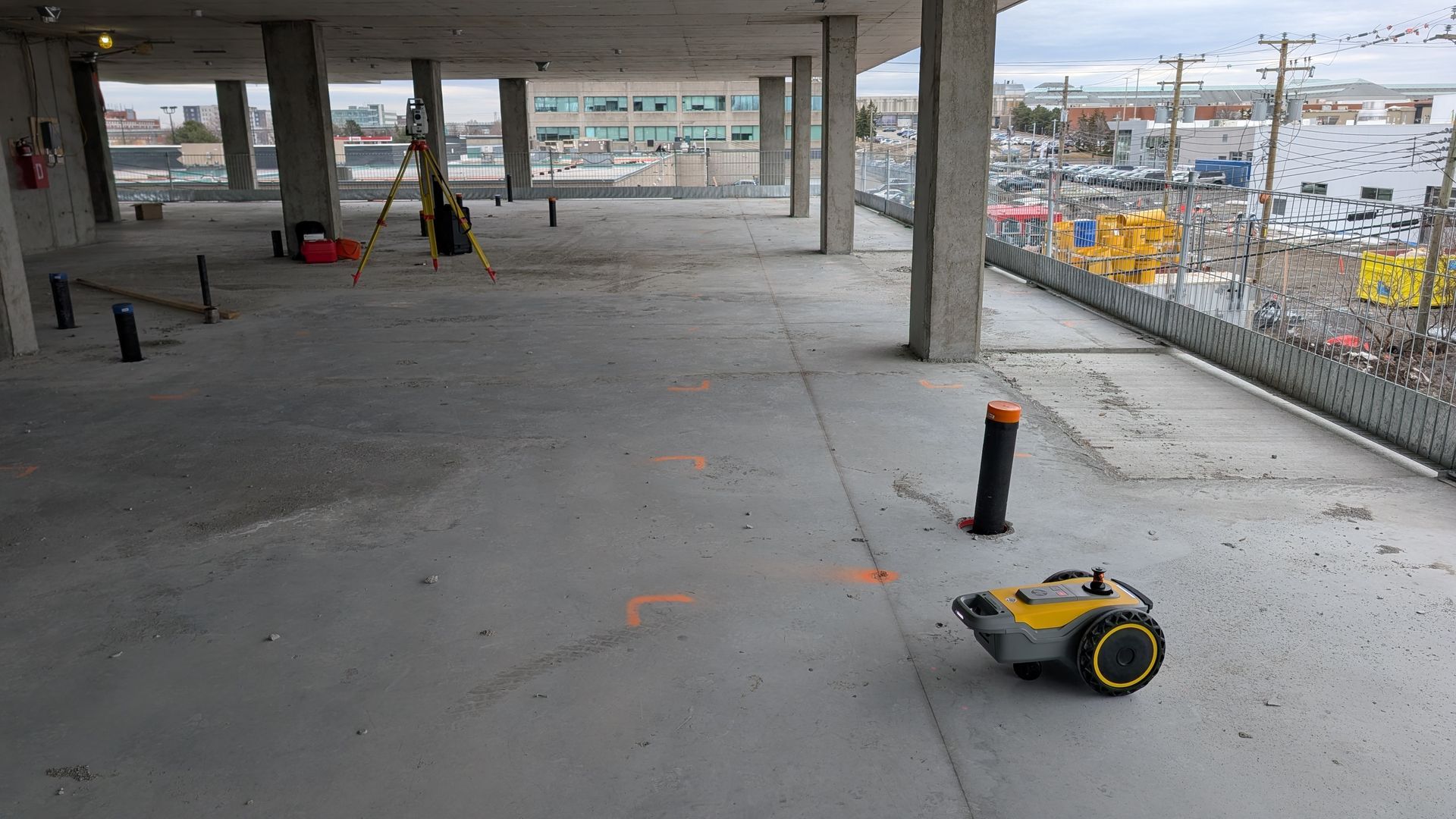 Un sol de parking en béton avec du matériel de topographie jaune, des marquages ​​orange et des outils de construction.