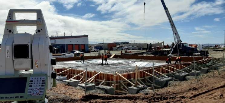 Un instrument de topographie au premier plan, surplombant un chantier de construction avec des fondations en béton et une grue.