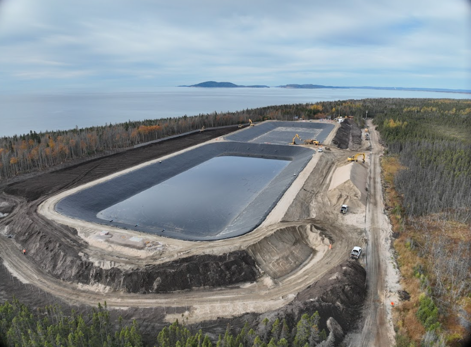 Vue aérienne de deux grands bassins de stockage d'eau revêtus, situés sur une côte boisée à proximité d'un plan d'eau.