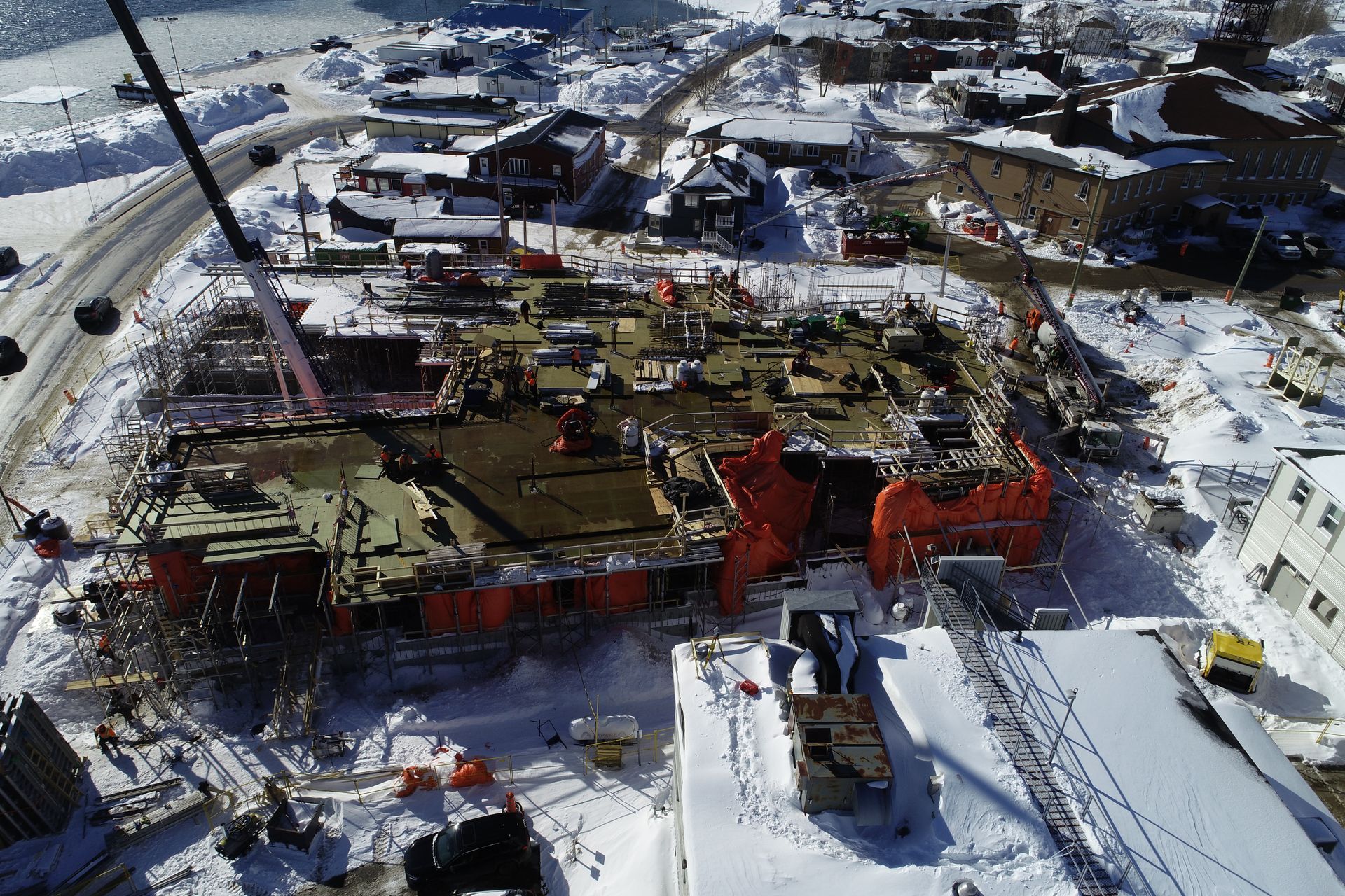 Vue aérienne d'un chantier de construction en activité, entouré d'une épaisse couche de neige, dans une petite ville isolée.