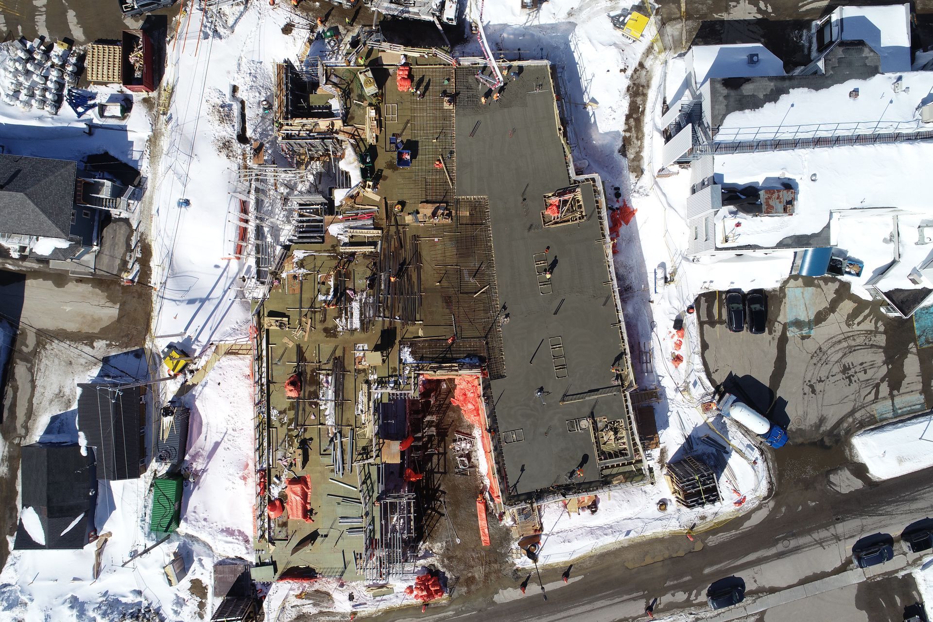 Vue aérienne d'un chantier de construction où des ouvriers coulent des fondations en béton, le tout entouré de neige.