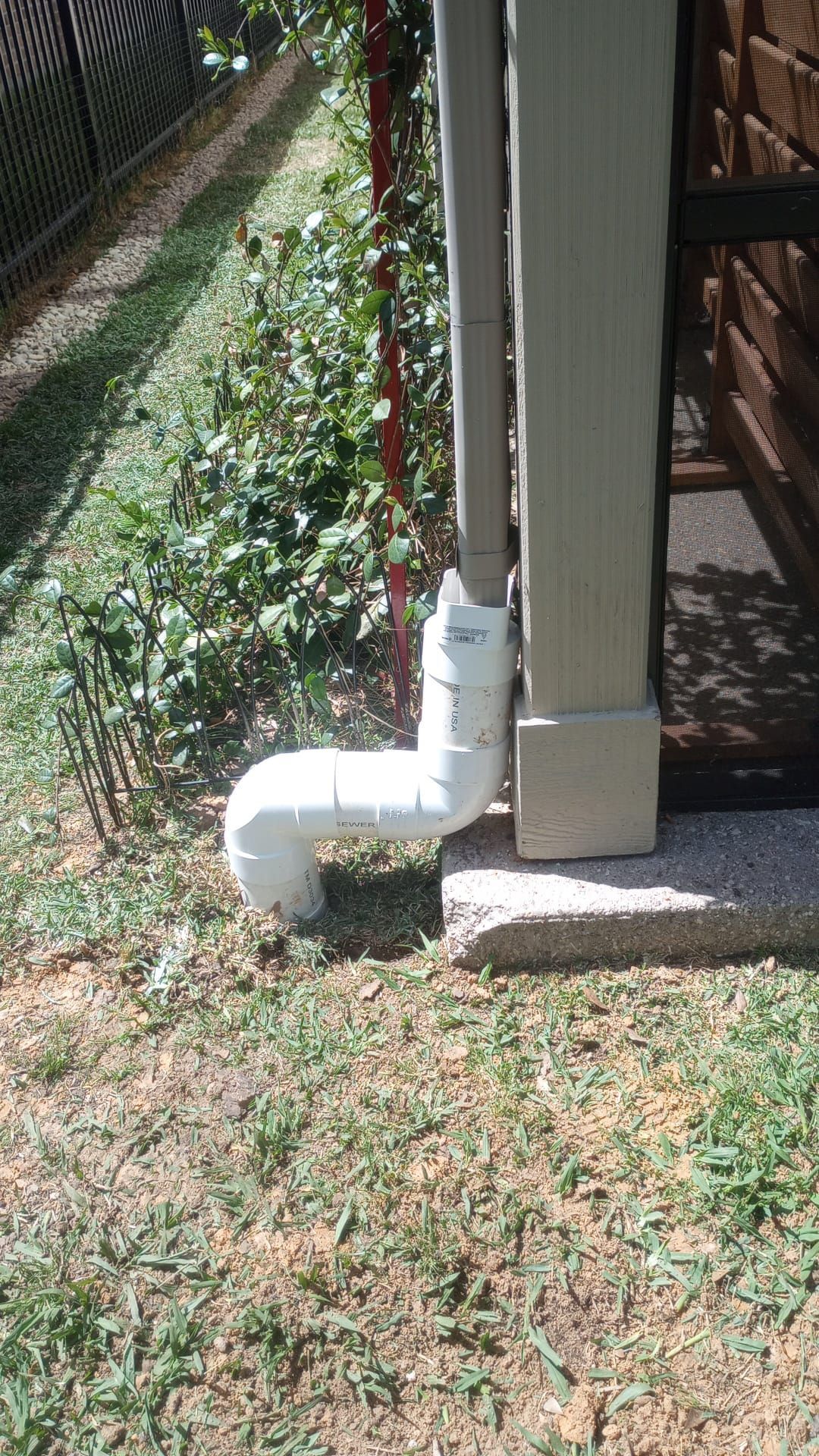 White PVC downspout extension directs water from a beige gutter onto the grass.