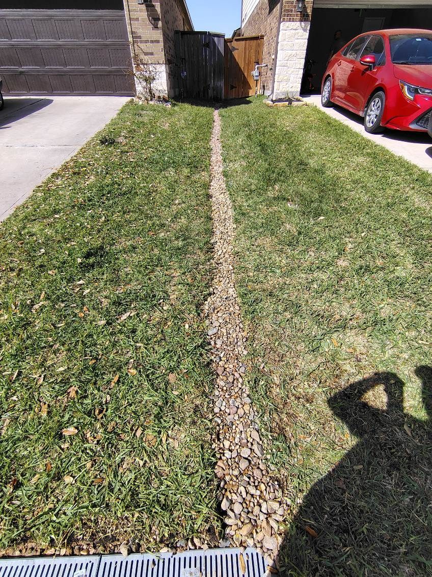 Grassy yard with gravel drainage channel; red car parked in driveway. Sunny day.
