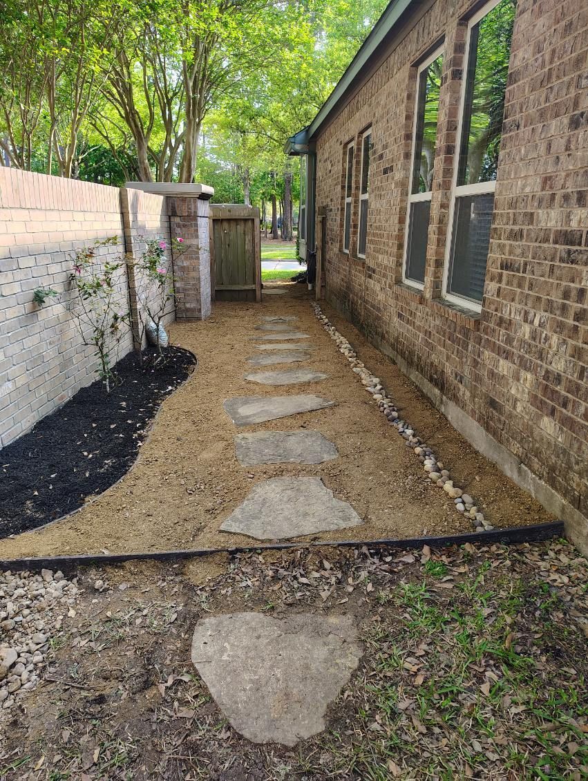 A stone pathway leads through a landscaped side yard next to a brick building.