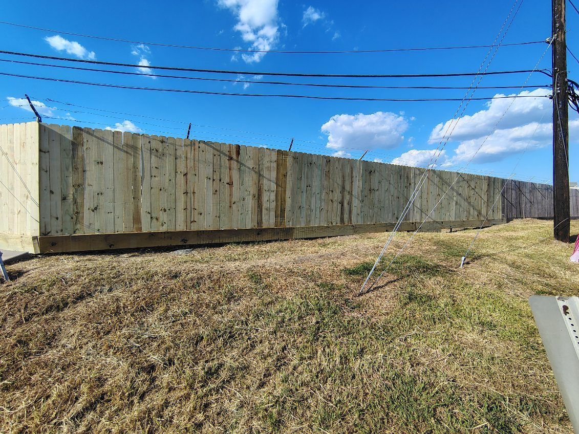 Long wooden fence in a grassy field against a blue sky with utility lines overhead.