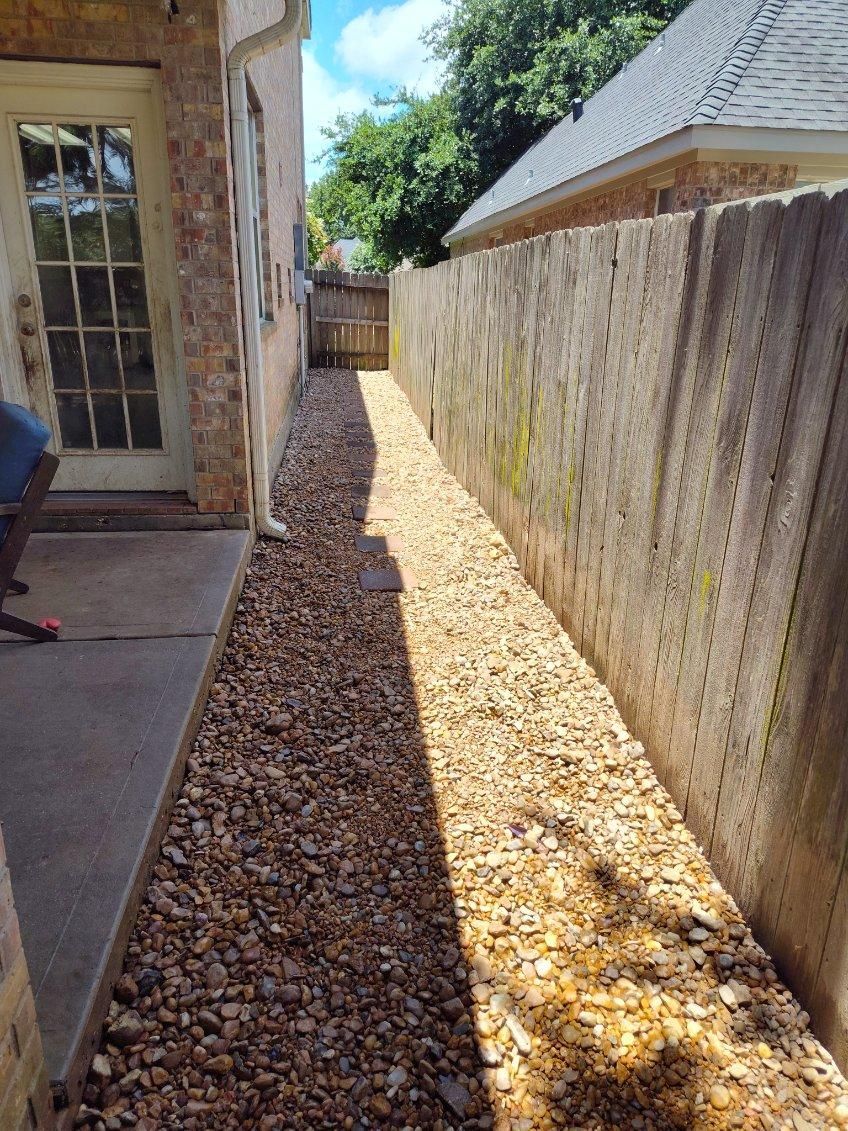 Gravel-filled side yard between a building and wooden fence, with a door and partial view of a person.