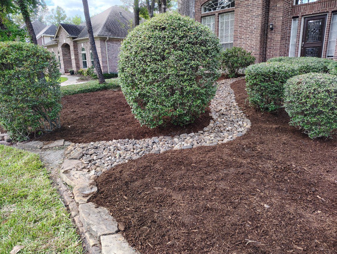 Landscaped front yard with green bushes, brown mulch, and stone edging.
