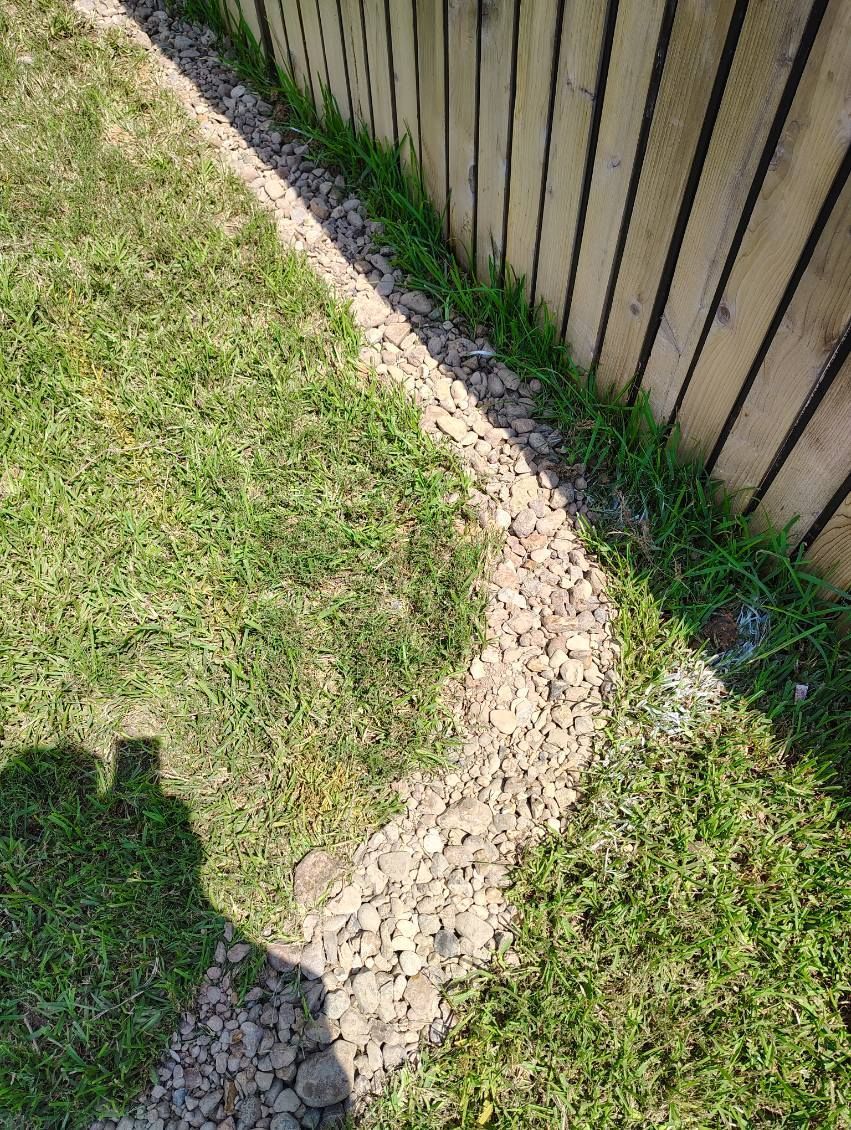 Gravel path bordering a wooden fence, curving through green grass on a sunny day.