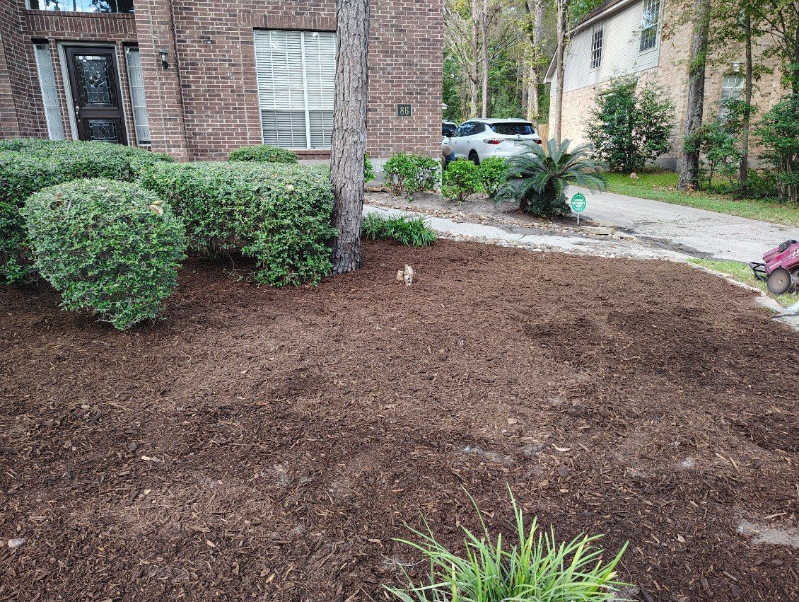 Mulched landscaping in front of a brick building and trimmed bushes. A driveway and car are visible in the background.