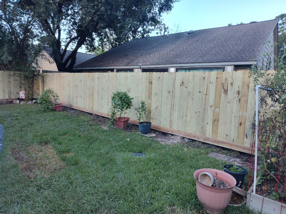 Wooden fence in a yard with grass, potted plants, and a house in the background.