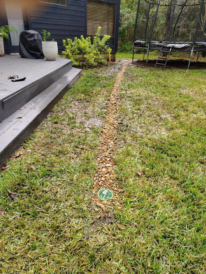 A gravel-lined drainage channel in a grassy yard, next to a patio.