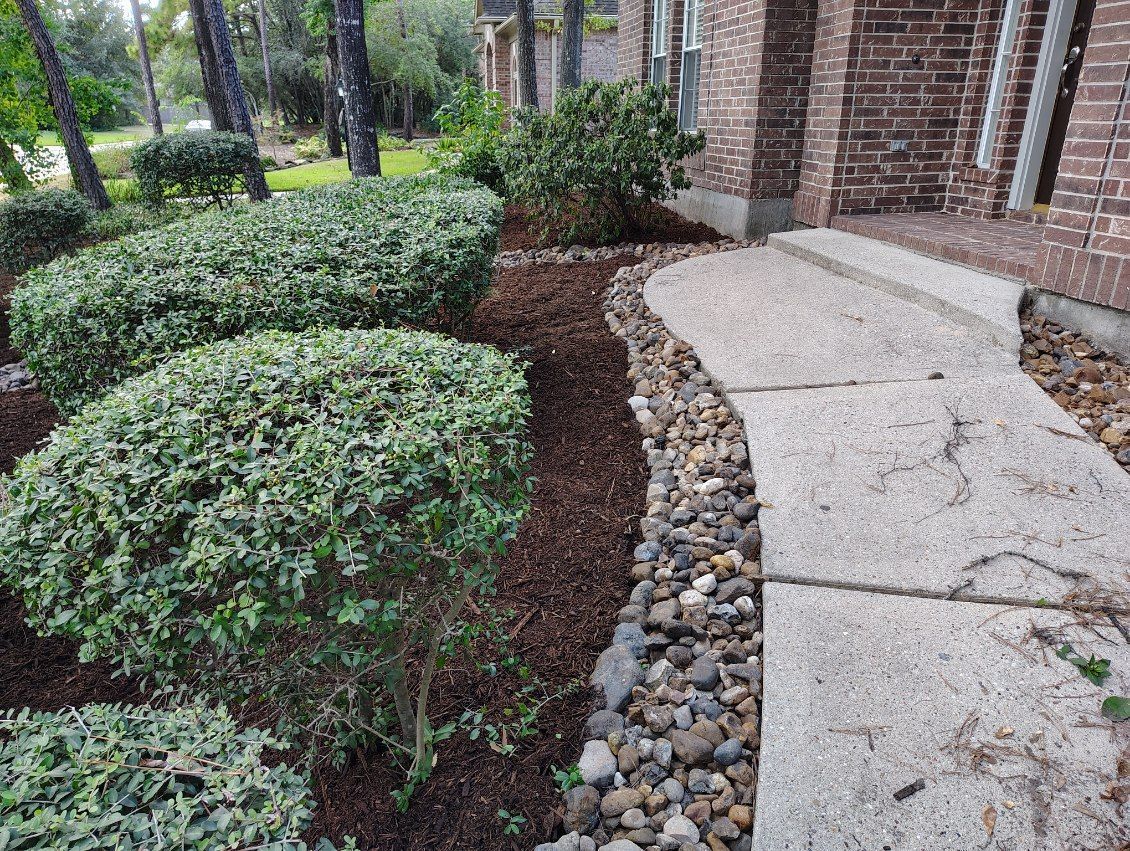 Stone path leading to a brick building, bordered by mulch, pebbles, and trimmed green bushes.