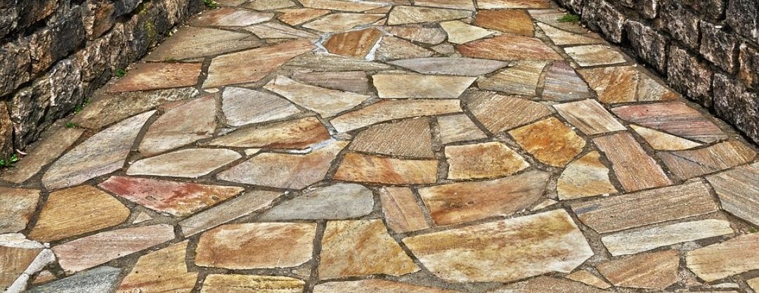 Stone pathway with varying shades of brown and gray stones, bordered by brick walls.