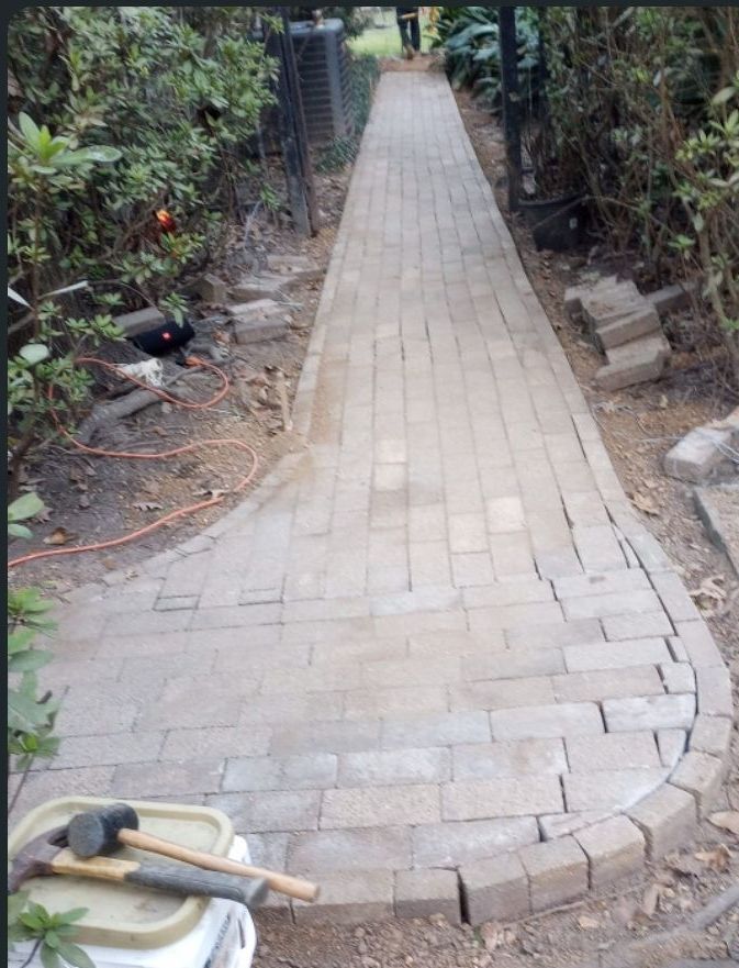 Brick pathway curves through a garden, with tools and plants visible.