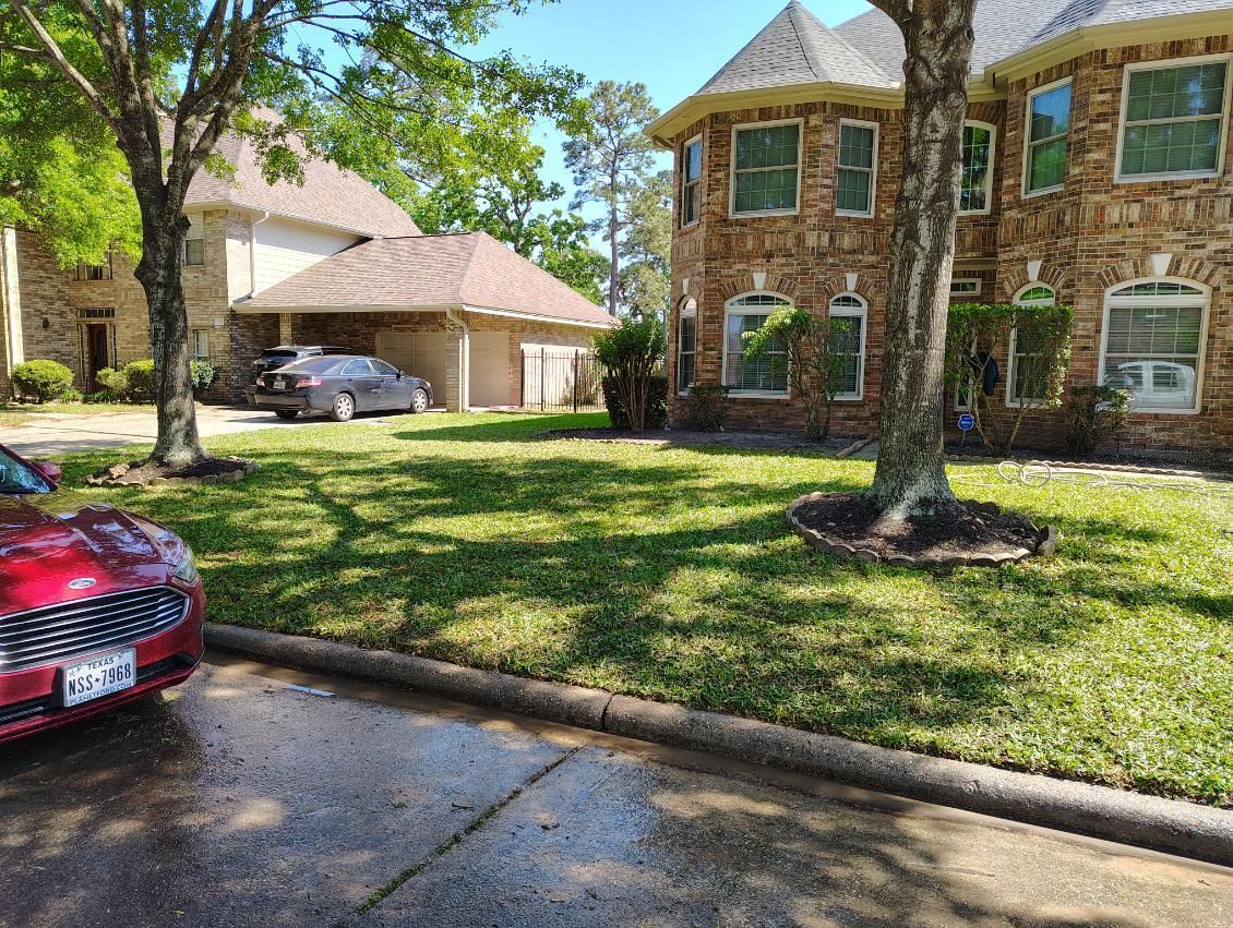 Two-story brick home with a well-maintained lawn, a red car in the foreground, and a garage in the background.