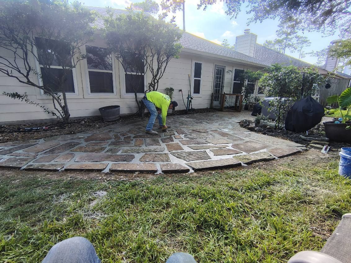 Person in neon shirt laying brick pavers on a patio in front of a house.