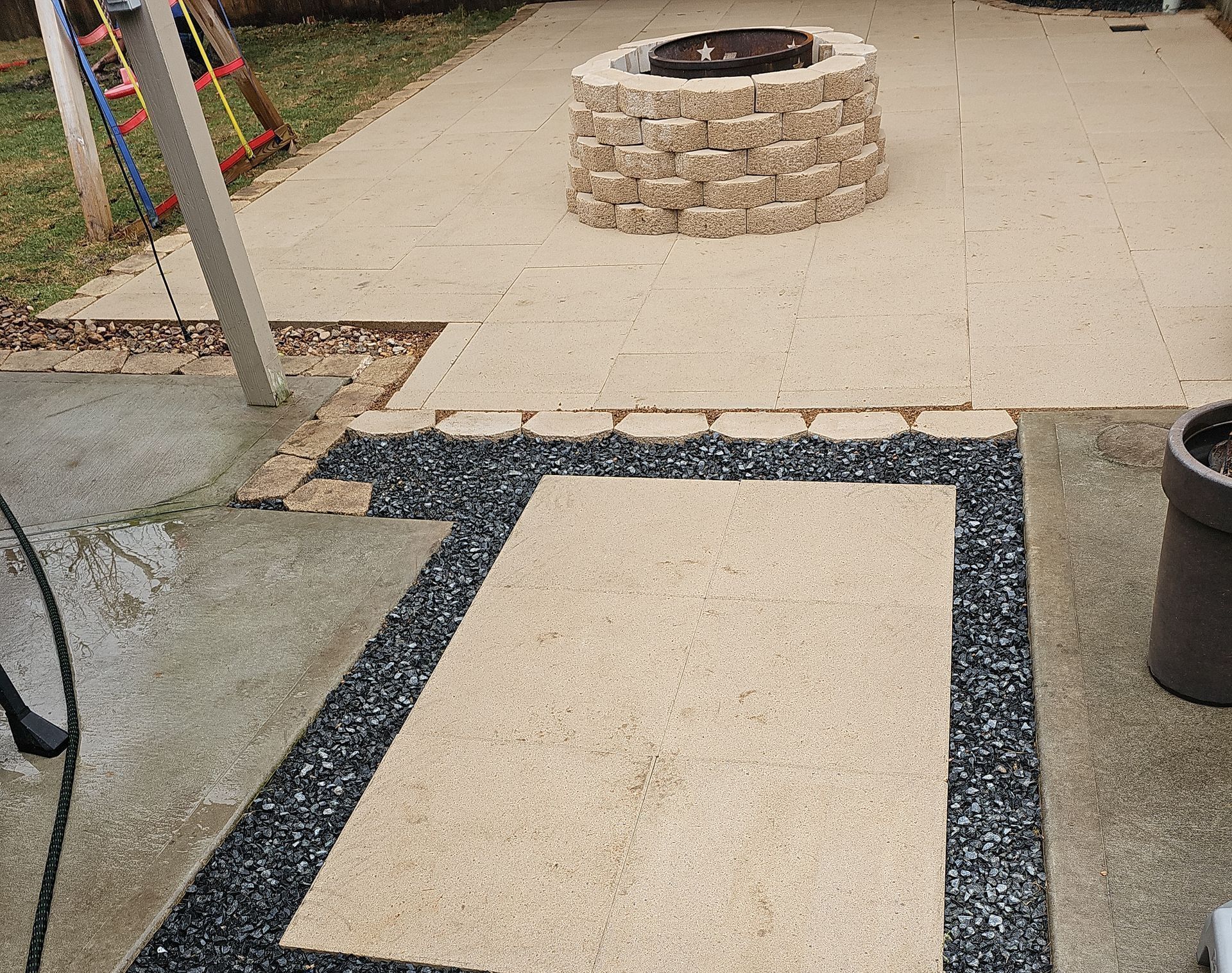 A patio with a fire pit. A stone path with black gravel border and tan pavers.