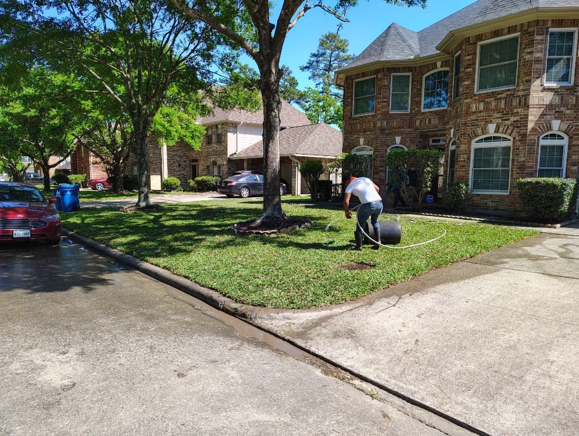 Man rolling lawn roller on green grass in front of brick house.