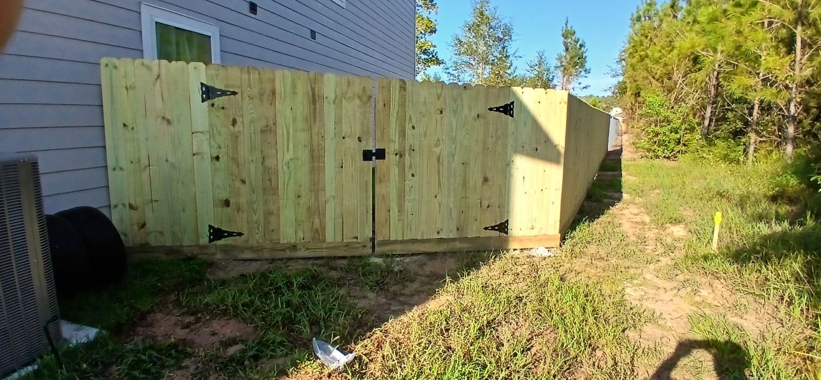 Wooden fence with a gate, next to a building and grassy area.