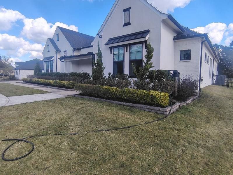 White house with dark roof and trim, green lawn, and neatly trimmed hedges.