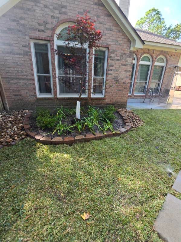A brick home with a small tree and flower bed in the front yard.