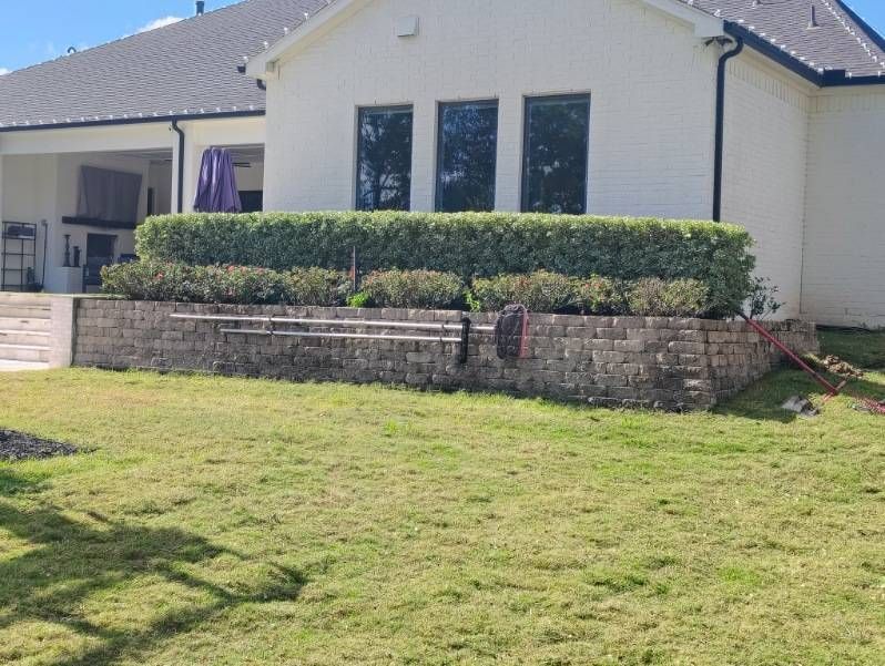 White house with brick retaining wall, green lawn, and hedge.