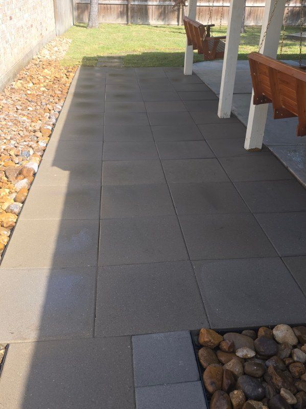Patio paved with dark gray tiles, adjacent to a rock garden and a grassy yard under a covered seating area.