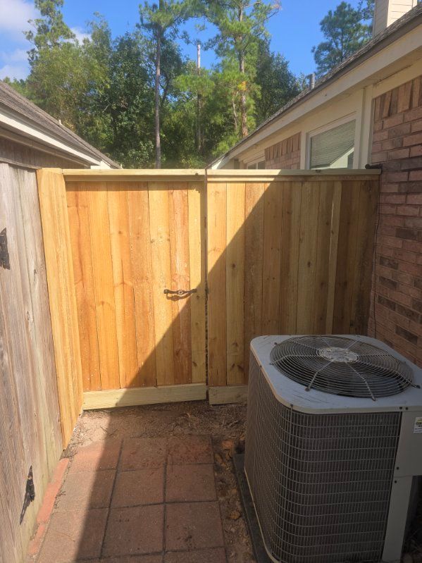 Wooden gate enclosing a small patio with an AC unit and brick pavers.