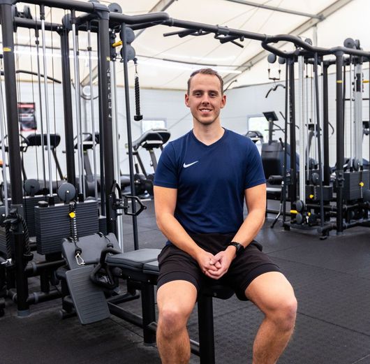 Een man in een blauw shirt zit op een bankje in een sportschool